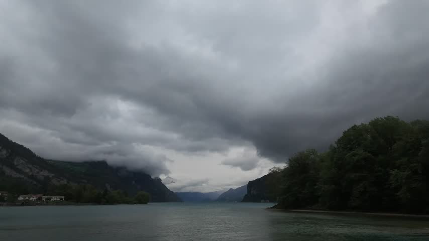 Weesen, Walensee, Switzerland, timelapse of dark storm clouds moving over calm lake and misty mountains, moody weather.