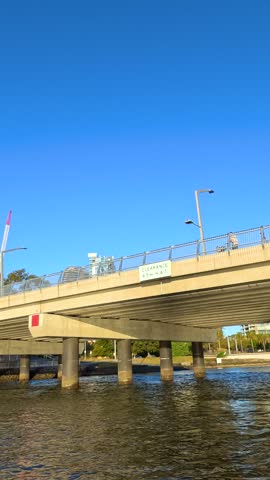 POV of a boat traveling under a concrete bridge towards the sunny Gold Coast skyline.