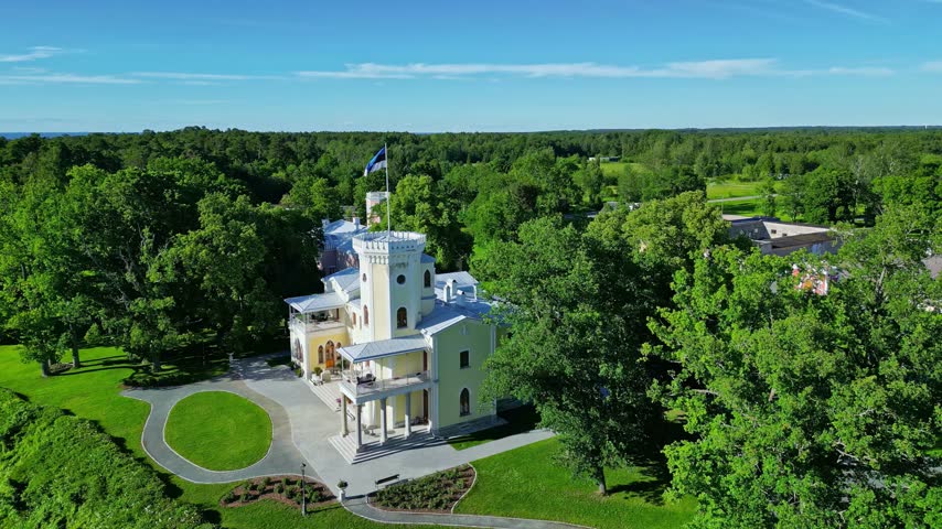 Aerial view of a historic manor house surrounded by lush green trees and a manicured lawn in Estonia.