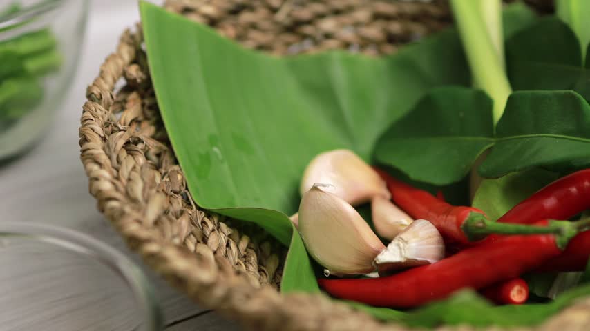 Hand in black glove picking garlic from a basket of Thai herbs