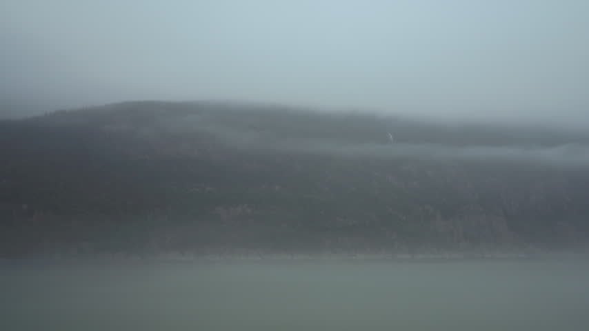 Fog over a forested mountainside with a small waterfall