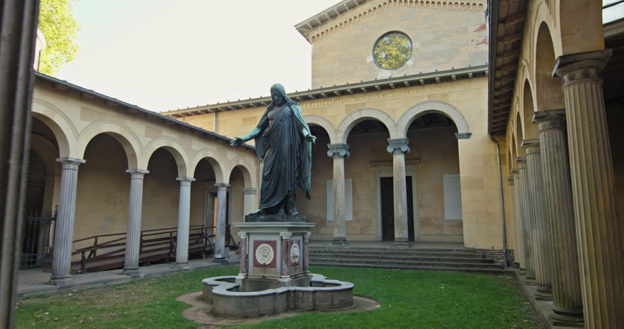 Bronze Christ statue in the Friedenskirche courtyard, Sanssouci Park, Potsdam, Germany, with church arcades behind.