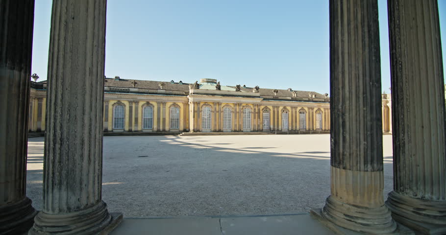 The north courtyard of Sanssouci Palace in Potsdam, Germany, with its long yellow facade and curved colonnades.