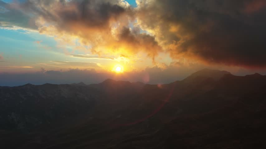 Aerial view of Durmitor National Park at sunset with dramatic clouds over the rugged mountain peaks during the golden hour in Montenegro.