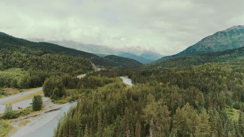 Highway and turquoise river through a forested Alaska valley aerial