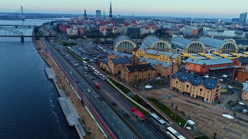 Aerial view of the historic Riga Central Market buildings, the Daugava River, and the surrounding urban cityscape with traffic on the road in Latvia.