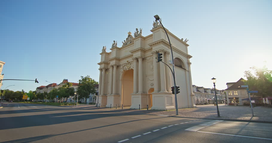 Brandenburg Gate draws visitors to Luisenplatz in Potsdam, Germany, through neoclassical arches in golden-hour light.