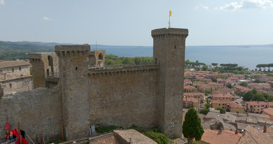 Panorama of the walls and main tower of the Rocca Monaldeschi with a flag on top, overlooking the town and Lake Bolsena, in the province of Viterbo, in Lazio, Italy, on a sunny summer morning.