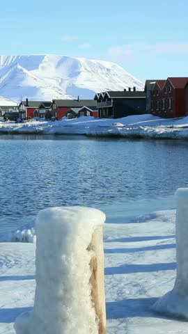 Wooden houses of Longyearbyen town on the snowy shore of the Arctic Ocean with snow-capped mountains in the background in Svalbard Norway