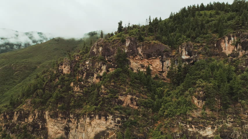 Rocky cliff and forested hills with low clouds aerial