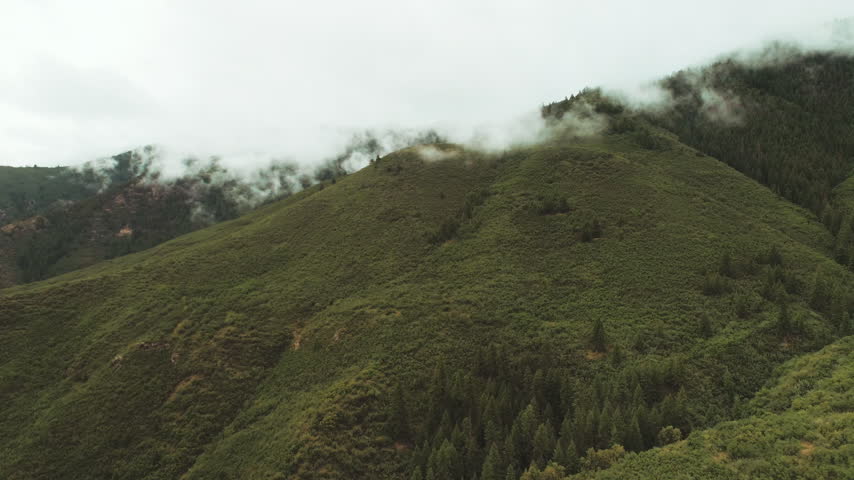 Low clouds rolling over a green mountain ridge aerial
