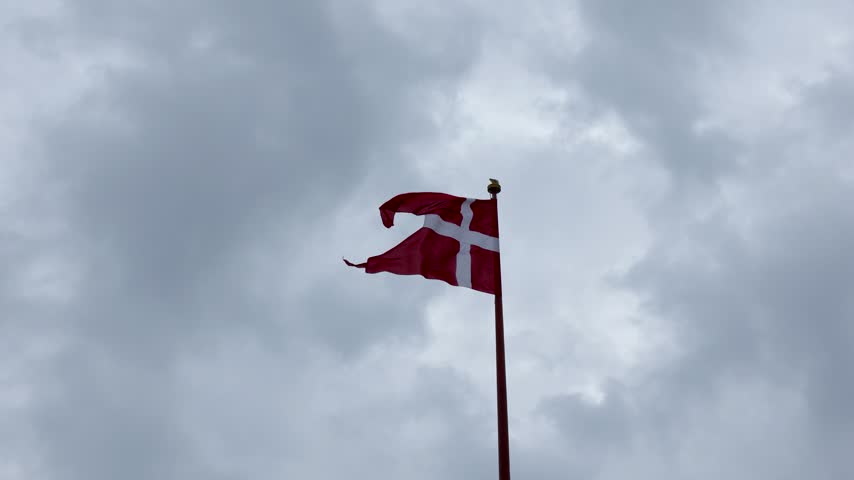 Danish national flag waving against a cloudy sky above Copenhagen, Denmark