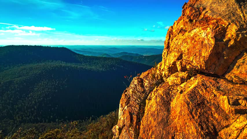 Golden sandstone cliffs above forested mountains at sunset.