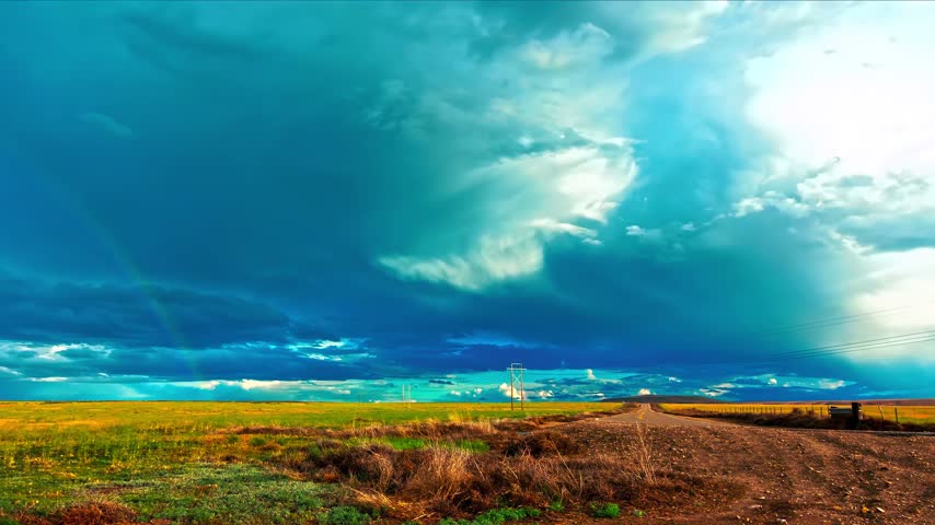 Cloud time lapse over an open field and dirt road.