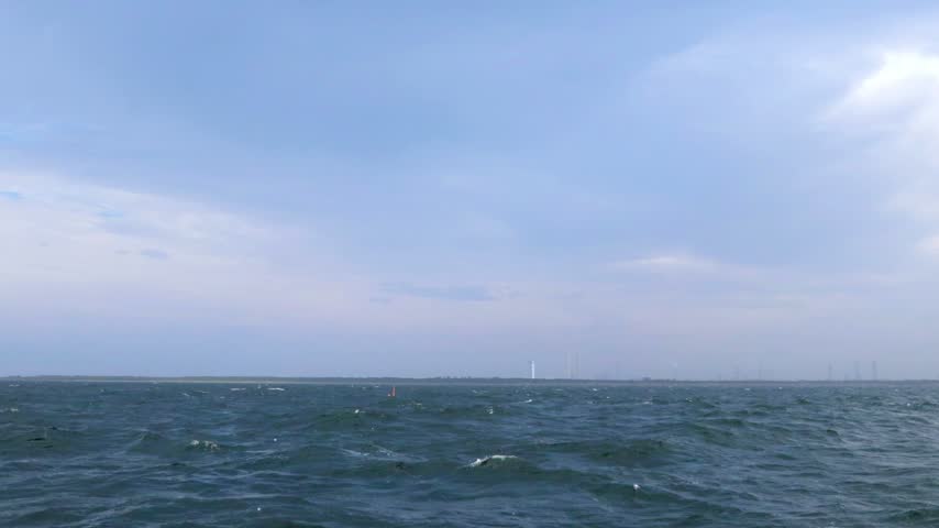Choppy blue sea with small whitecaps beneath a cloudy sky, with a distant industrial shoreline along the horizon in Yokohama, Japan.