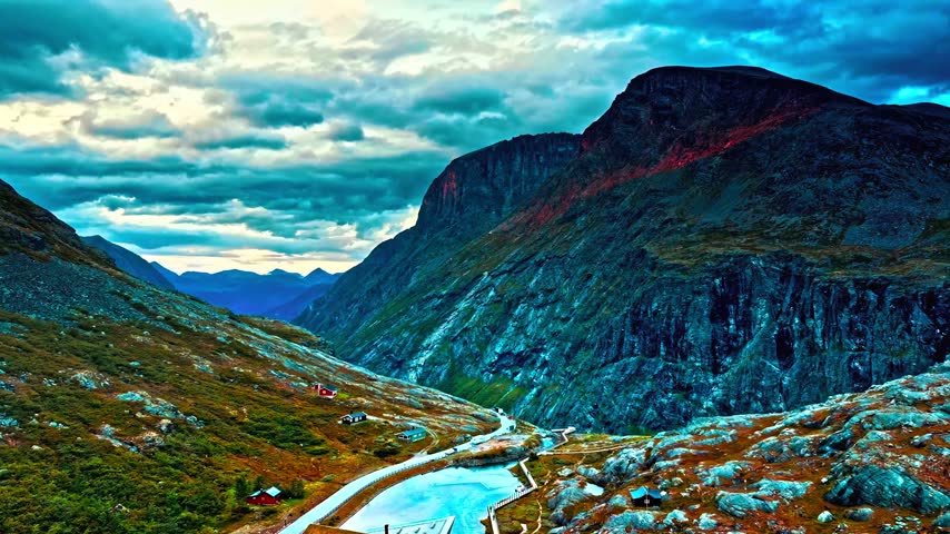 Aerial view of winding road and icy river in a mountain valley.