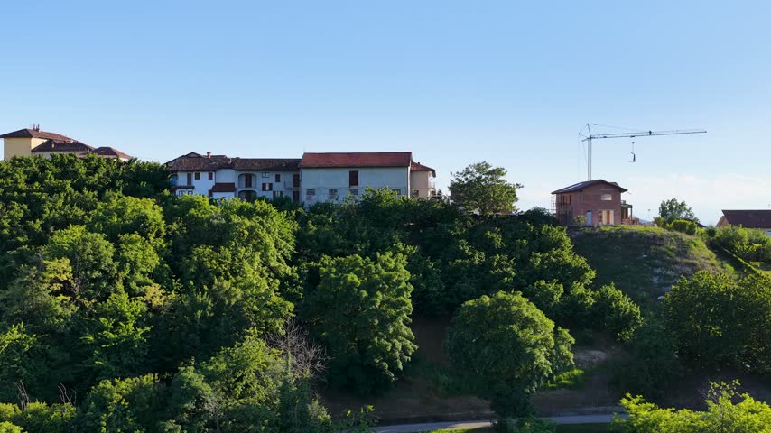 Rising aerial view of a picturesque Italian village perched on a green ridge in Piedmont.