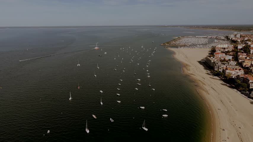 Yachts on buoys and speedboat wakes in the Arcachon Basin, Gironde, France, between the town beach, seafront apartments and the marina breakwater.