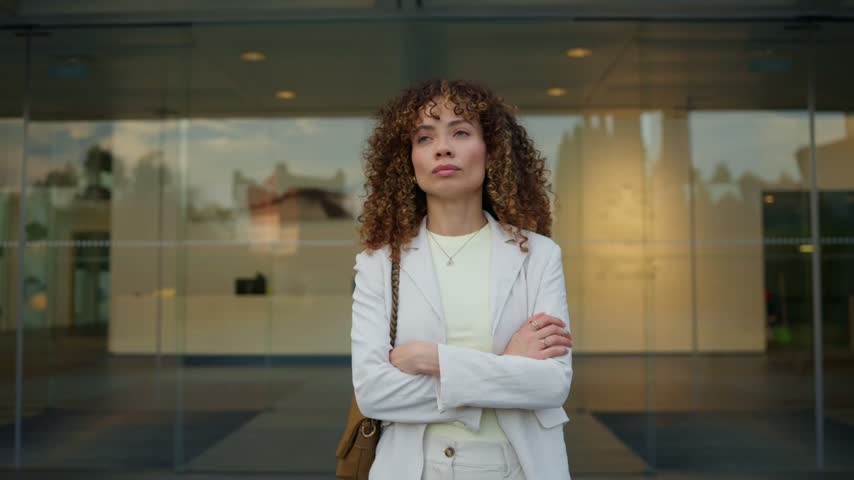 Businesswoman standing with crossed arms outside a modern glass office building