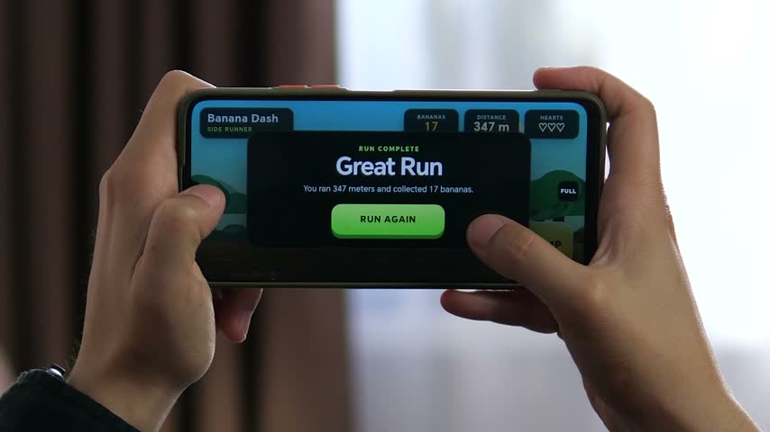 Person plays a colorful side-scrolling mobile game on a smartphone, collecting items and avoiding obstacles as casual gaming and mobile entertainment continue to grow.