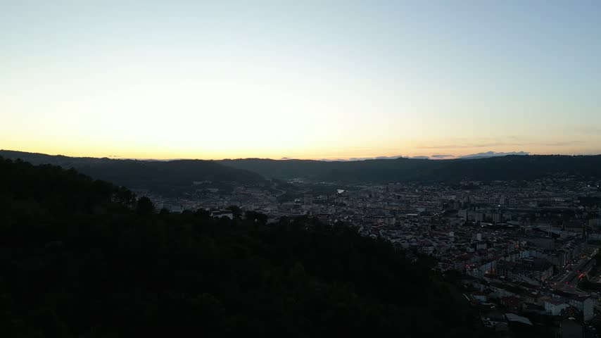 Ourense city beyond a dark wooded slope beneath a pale evening sky in Galicia, Spain, aerial