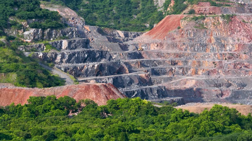 Industrial open pit limestone quarry carved into a mountain surrounded by dense green forest.