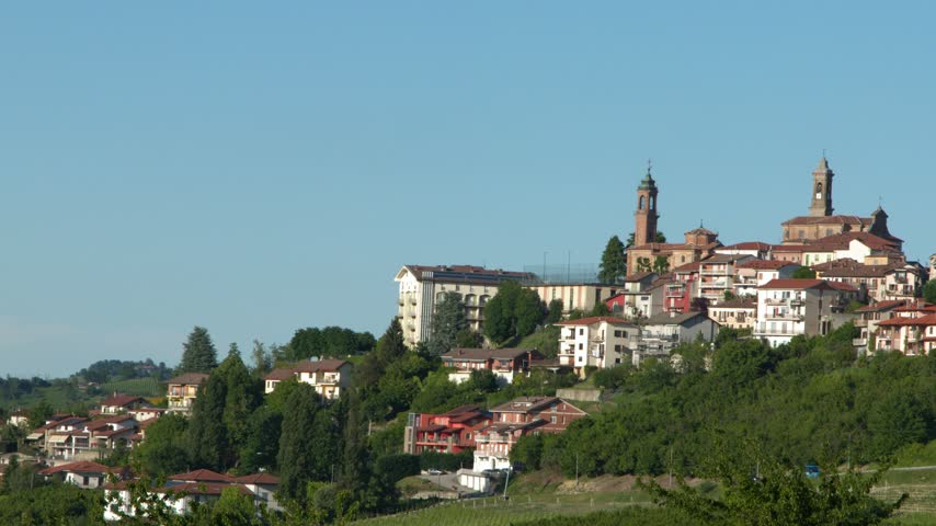 Pan across a historic Italian hilltop village with terracotta roofs and church towers in Piedmont.