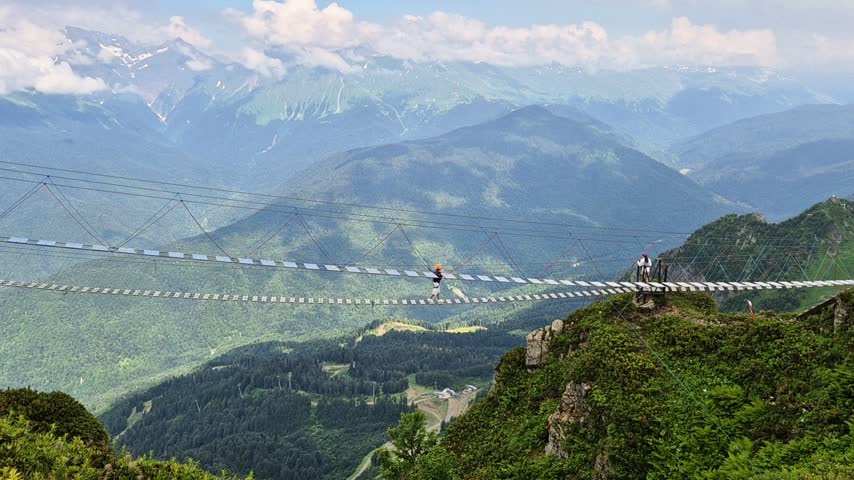 Extreme attraction at high altitude on the top of Aibga ridge, a rope suspension footbridge at Rosa Khutor mountain resort under a cloudy sky in summer. NotvAI.