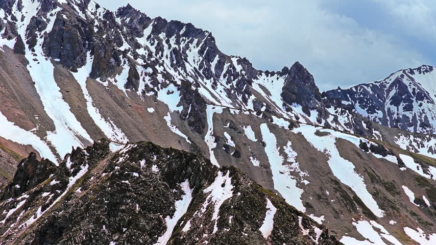 Majestic snow capped mountain peaks stretch across the rugged alpine landscape under overcast skies, captured in a telephoto shot.