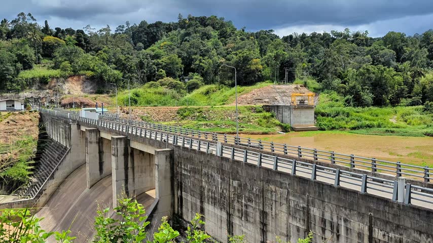 Truck driving over the Uma Oya reservoir dam bridge surrounded by green mountains in Sri Lanka
