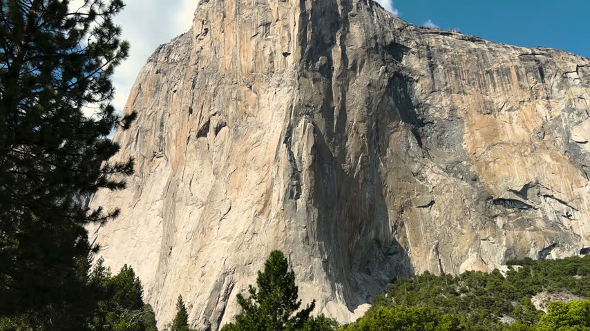 Low angle view of a towering granite cliff with pine trees in Yosemite Village, California