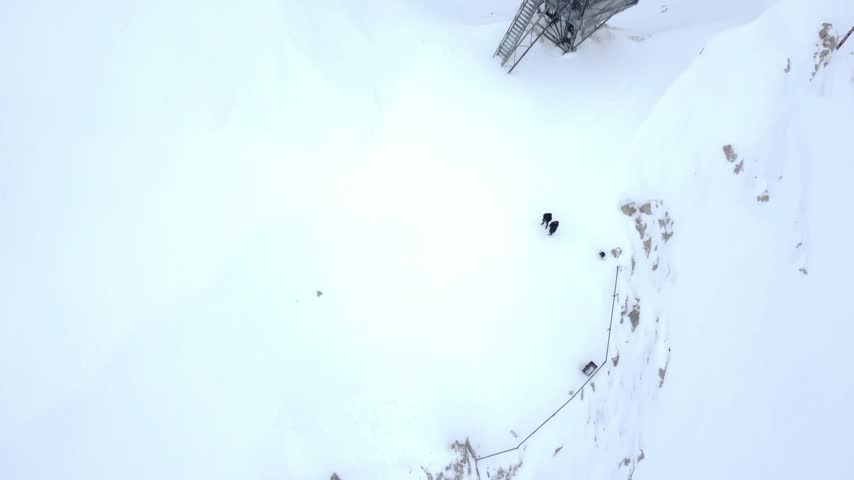 Aerial tilt up view from a weather mast beside the Hafelekar cable car station on the snowy Nordkette ridge, revealing Innsbruck far below, Tyrol, Austria