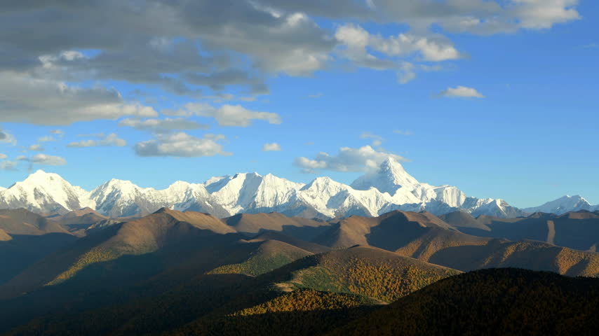 Scenic sequence of snow-covered Mount Gongga in Sichuan, China, showing layered mountain ridges, golden autumn forests, drifting clouds and pink light on the summit.