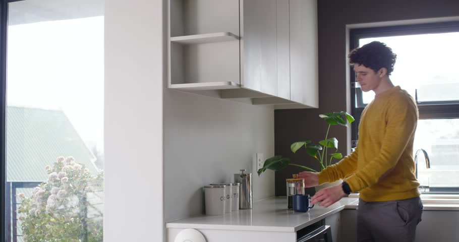 African-American man placing mug, pouring French press in kitchen, sipping, seeking calm. Minimalist, backlit, sunlit, window, home, coffee, brewing