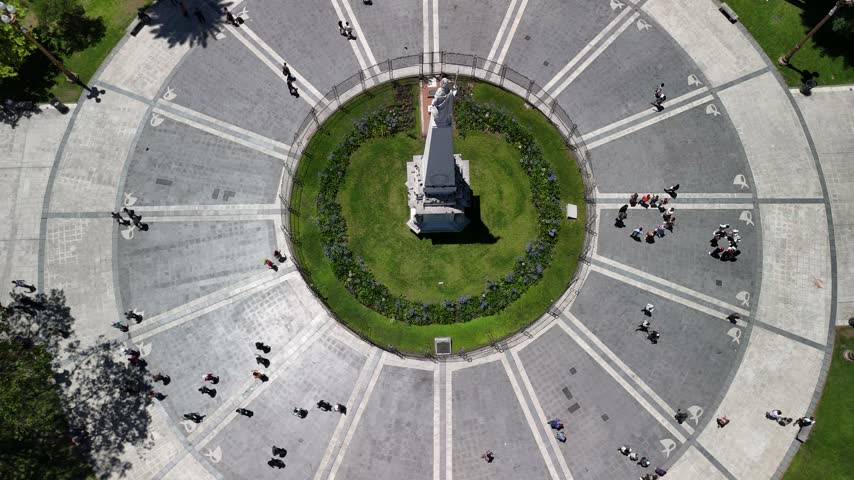 Aerial view of a circular plaza with a central monument surrounded by people walking on paved paths and green lawns in Buenos Aires, Buenos Aires, Argentina.