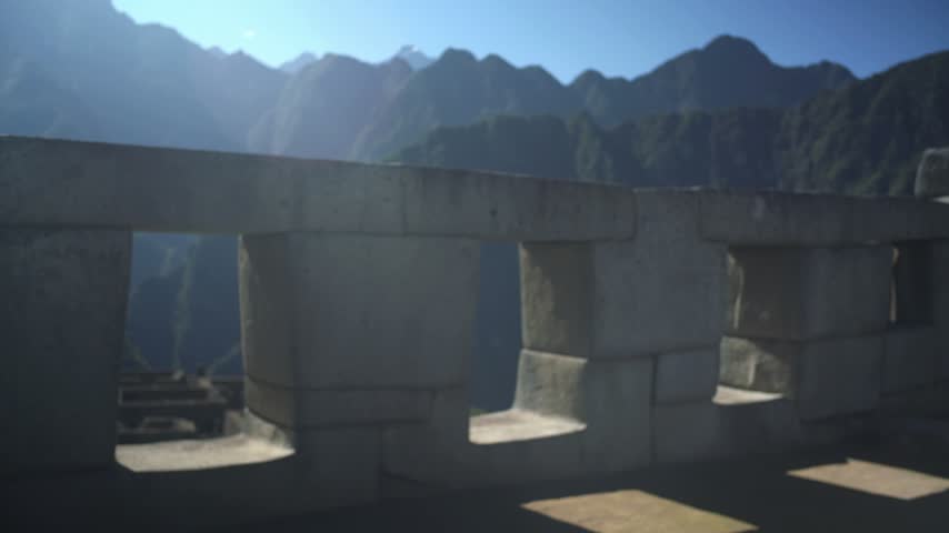 Sunlight falls through the stone openings of the Temple of the Three Windows at Machu Picchu with Andes mountains behind, Peru, Static Shot
