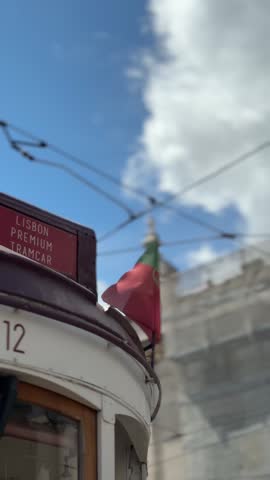 Close-up details of a historic red tourist tram displaying the Portuguese flag and "Lisbon Premium Tramcar" sign against a blue cloudy sky in Lisbon, Portugal.