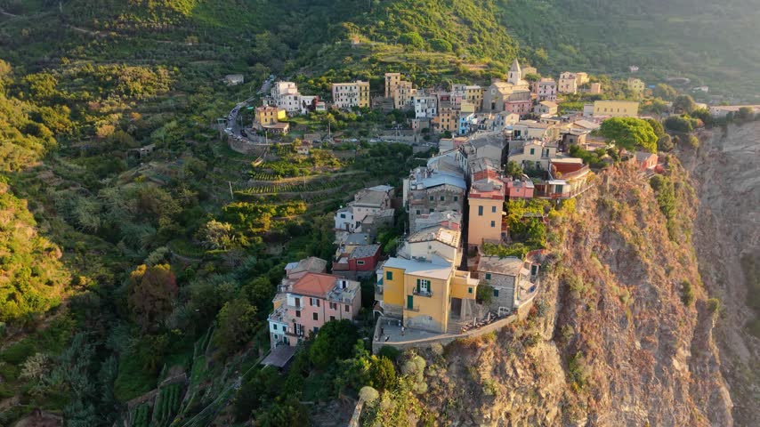 Aerial view of Corniglia village in Cinque Terre Italy during beautiful sunset. Colorful houses sit dramatically on top of steep rocky cliff. Ancient houses of Corniglia village in Italy