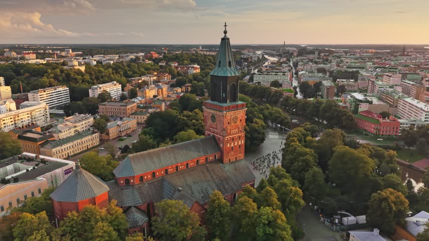 Aerial view of Turku Cathedral in Finland during beautiful warm golden hour. The historic red brick church stands tall beside the peaceful Aura river. Iconic Turku Cathedral and surrounding urban land