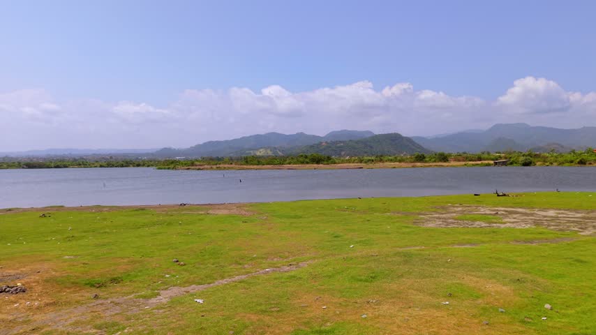 Scenic landscape of a calm lake with green grass foreground and mountain background under a blue sky
