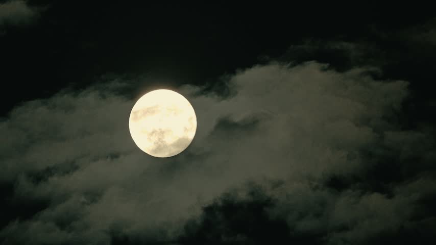 Bright full moon visible through drifting clouds against dark night sky, lunar features clearly shown, scene set during nighttime with atmospheric cloud cover, celestial event