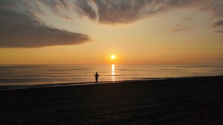 Silhouette of Woman Standing on Beach at Sunset.