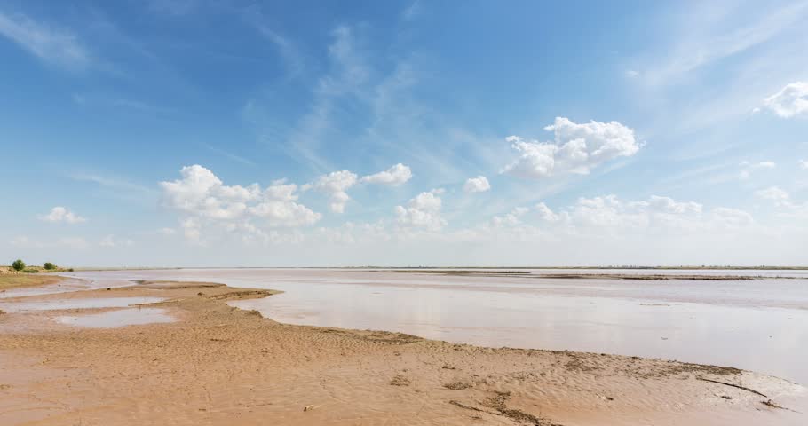 Time-lapse of the Yellow River flowing past sandy banks under blue sky with drifting white clouds, Bayannur, Inner Mongolia, China
