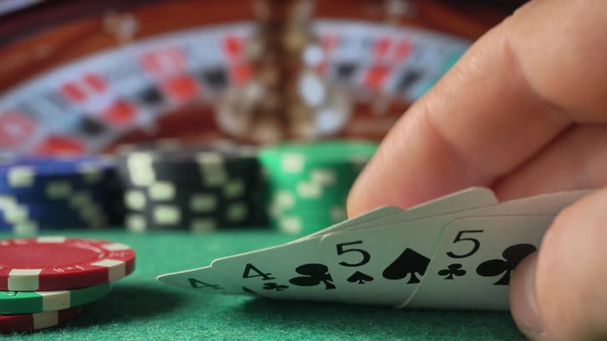 A hand fans four playing cards showing fours and fives beside stacked poker chips as the cards shift slightly on green felt at a casino table