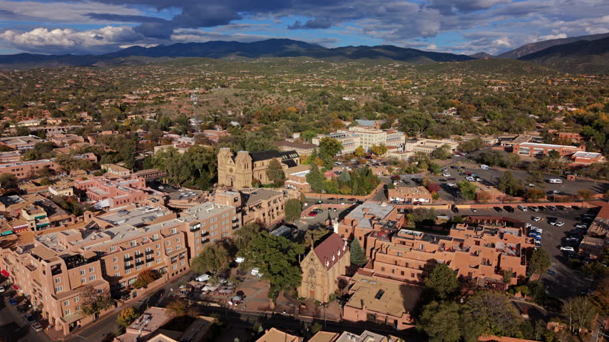 San Loretto chapel in Santa Fe, capital of New Mexico, USA. Aerial view of the Gothic church spire, adobe hotels and Cathedral Basilica, dark clouds over autumn hills and Sangre de Cristo Mountains.