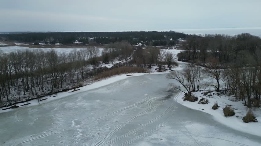 Aerial drone view of a frozen river bend between snowy banks and bare trees