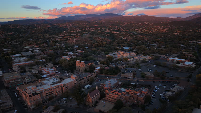 Dusk over Santa Fe, capital of New Mexico, USA. Aerial of Cathedral Basilica and Loretto Chapel among adobe hotels and parking lots. Pink clouds glow above the dark Sangre de Cristo Mountains.