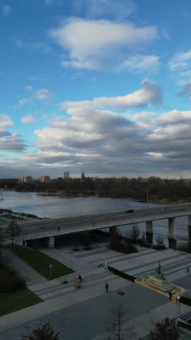 Aerial footage reveals a cable stayed bridge crossing the river as clouds drift above a riverside plaza, walkways, and distant skyline