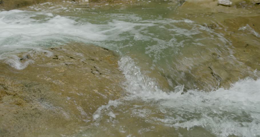 Close-up shot of water flows over smooth rocks. Slow motion.