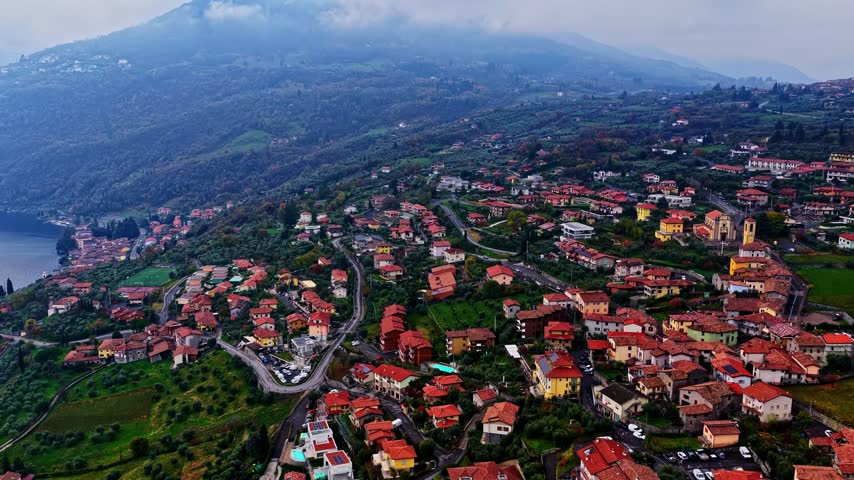 Aerial view of Lake Iseo and hillside town with red-roofed houses and a church overlooking the water in Lombardy, Italy.
